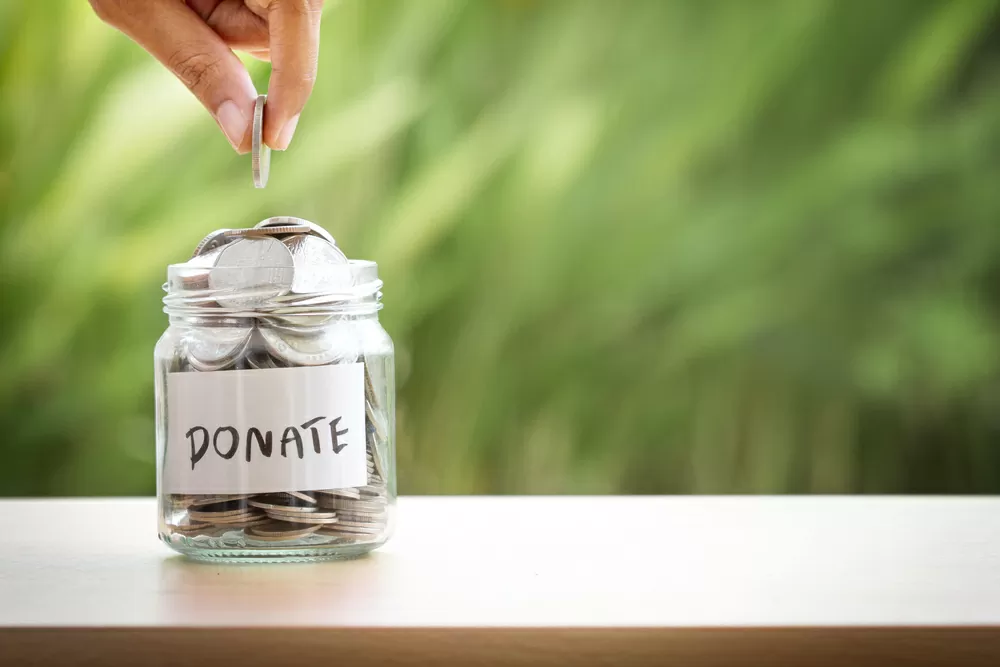A hand dropping a coin into a donation jar