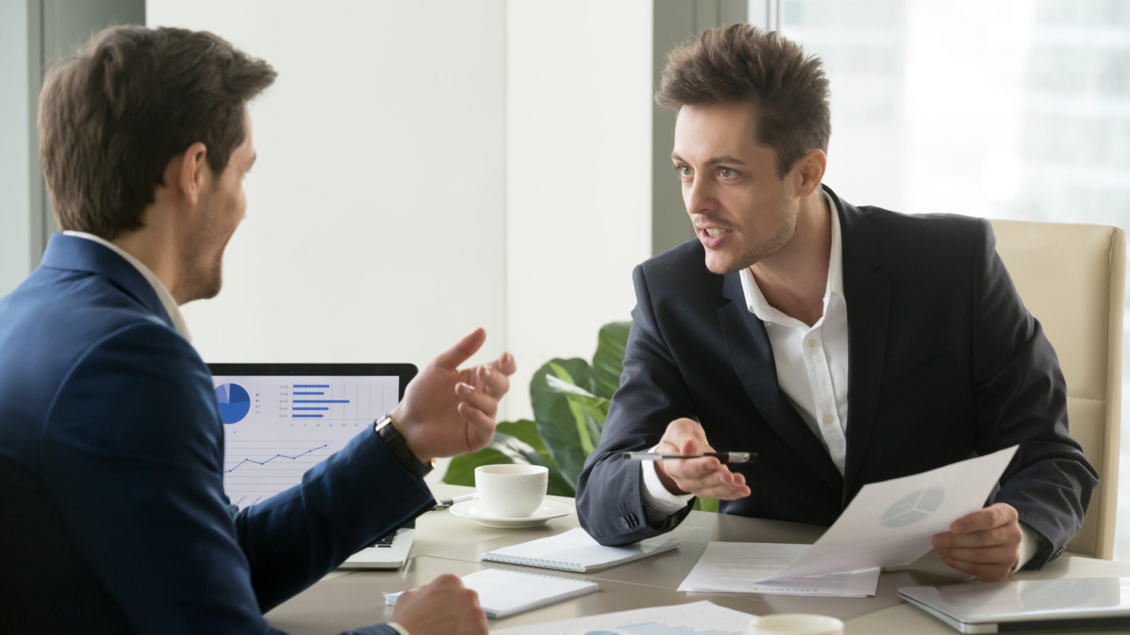 Two successful businessmen discussing company financial strategy, analyzing economic indicators, planning profitability and stock value growth while sitting at desk in office during business meeting