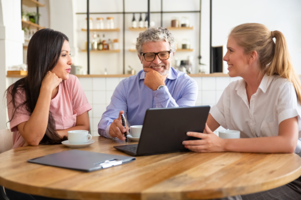 Happy female manager presenting project on laptop to young woman and mature man, discussing content with satisfied customers. Consulting or communication concept