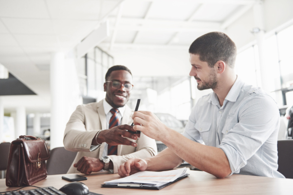 A young attractive black businessman buys a new car, he signs a contract and takes the keys to the manager.